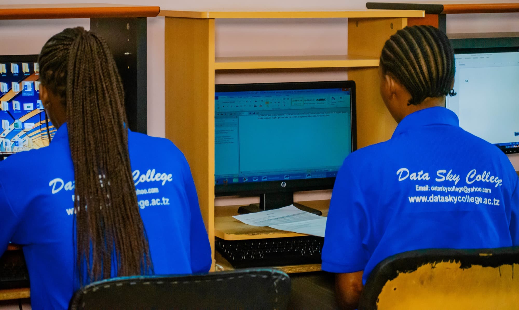 Two Datasky College students in blue college polo shirts working at a desktop computer in the college lab